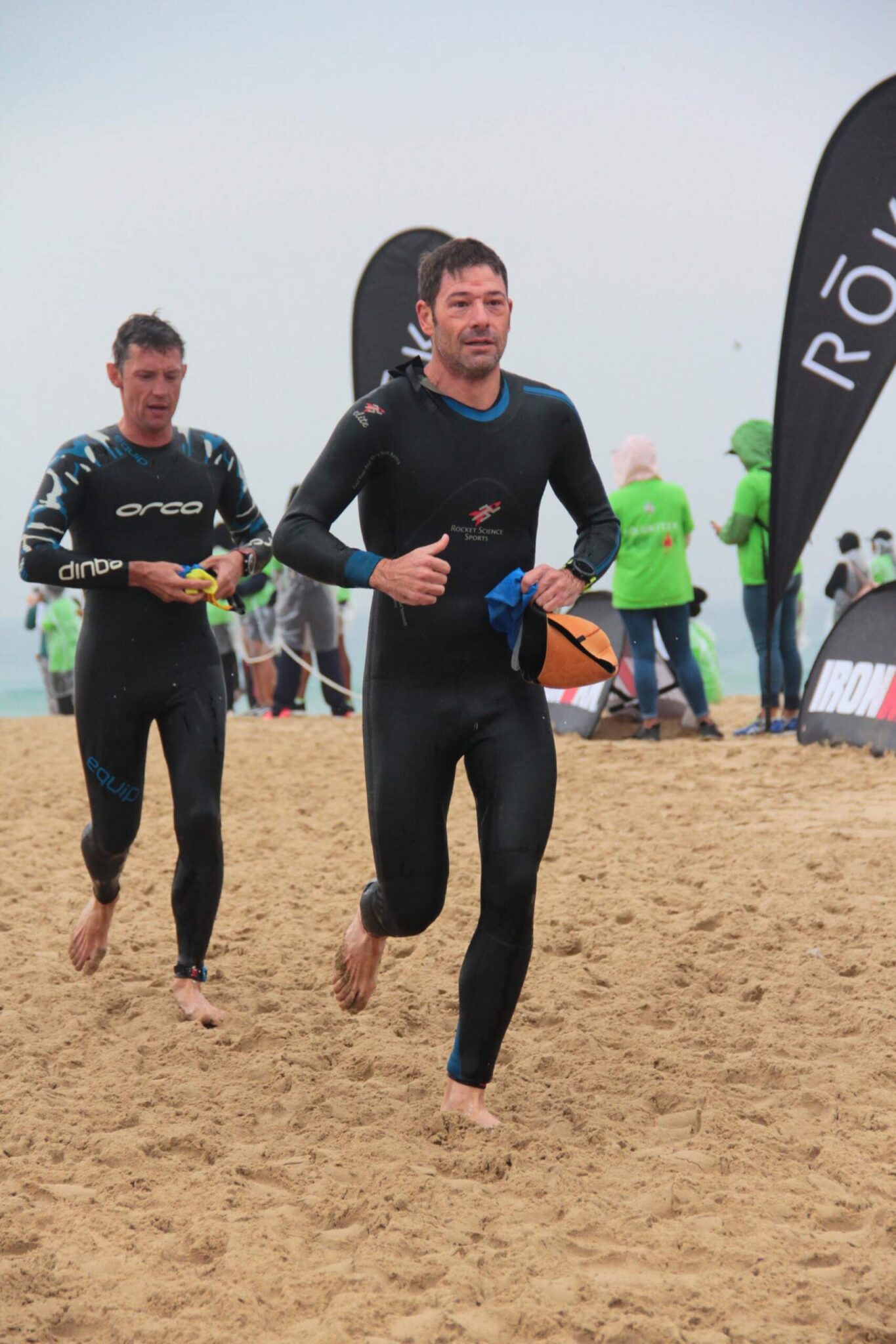 Ironman athletes exiting the water and running on a beach after a swim
